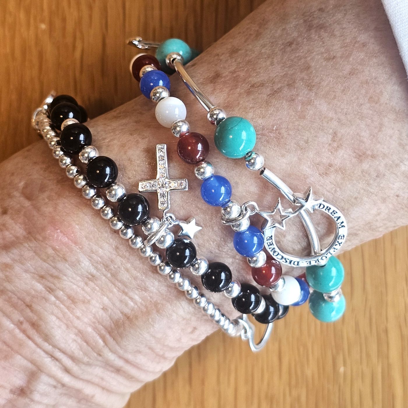 Wrist adorned with Bessie Bae sterling silver gemstone bracelets featuring turquoise, onyx, and blue agate beads.