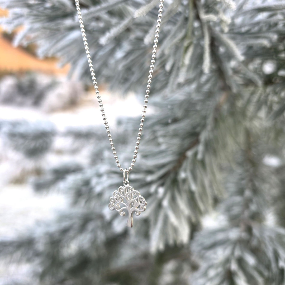 Sterling silver tree of life pendant necklace hanging from a frost-covered pine branch by Bessie Bae.