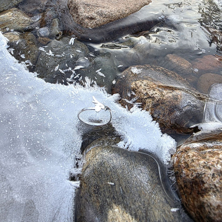 Sterling silver open ring resting on icy rocks beside a frozen stream in a winter landscape by Bessie Bae.