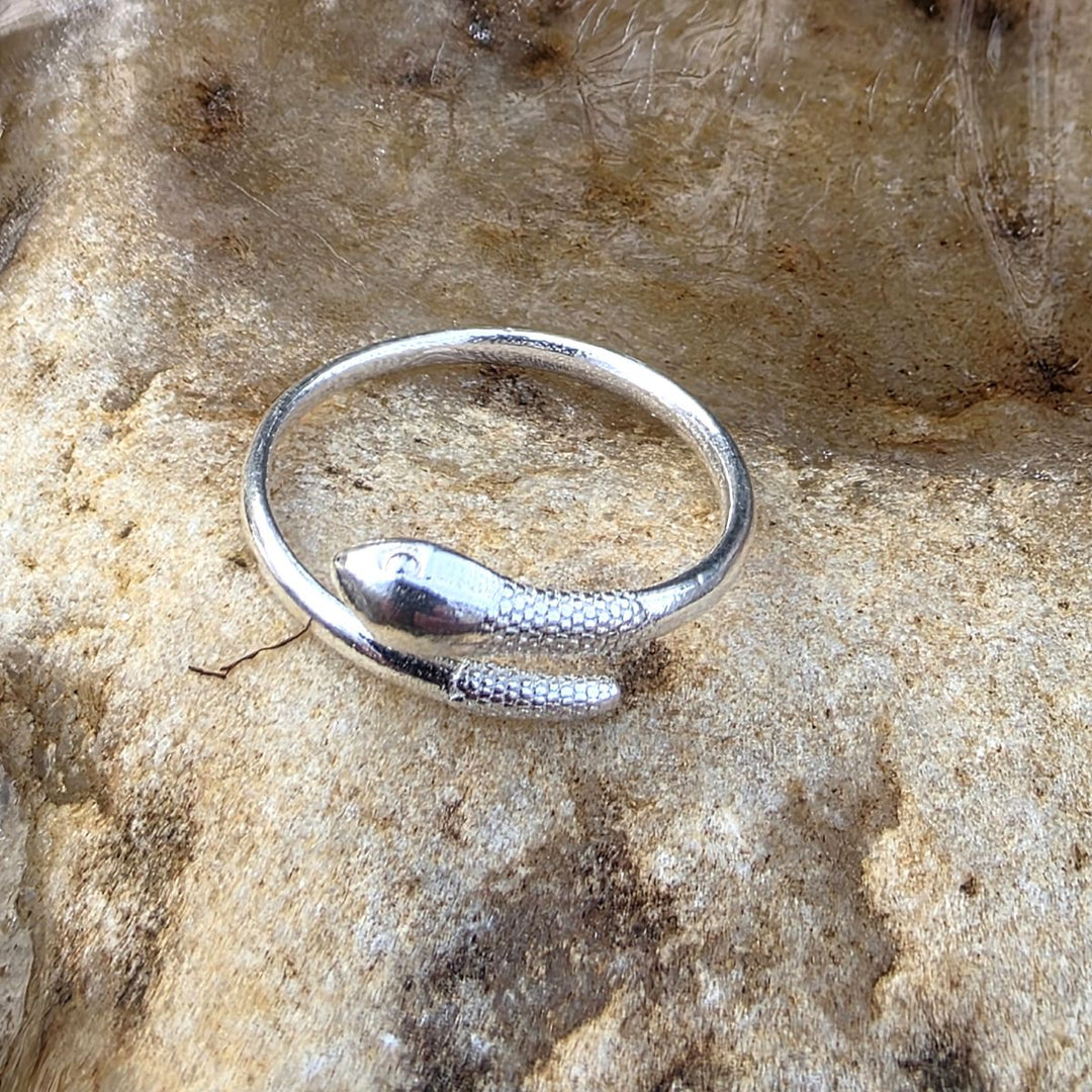 Sterling silver snake ring resting on natural stone, featuring a sleek wrap-around design with textured detailing inspired by nature by Bessie Bae.