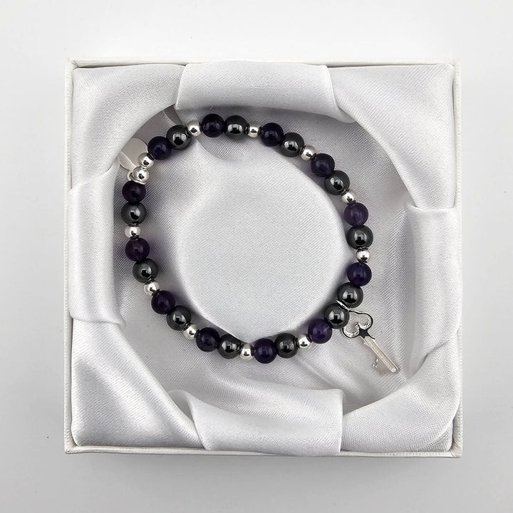 Top view of purple and silver gemstone bracelet with key charm in satin box.