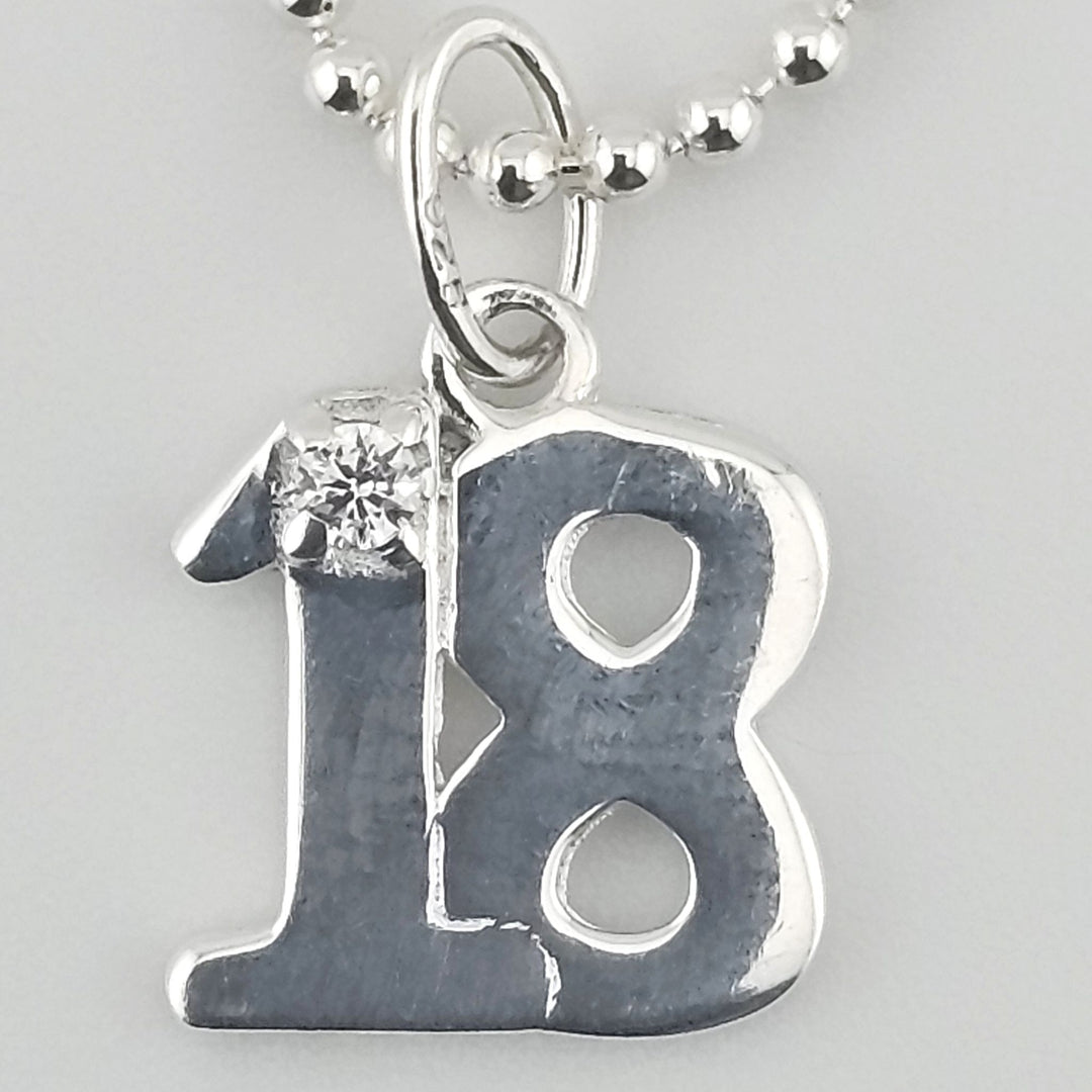 Close-up view of sterling silver ‘18’ pendant with sparkling stone detail.