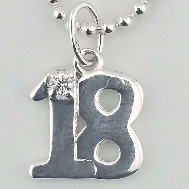 Close-up view of sterling silver ‘18’ pendant with sparkling stone detail.