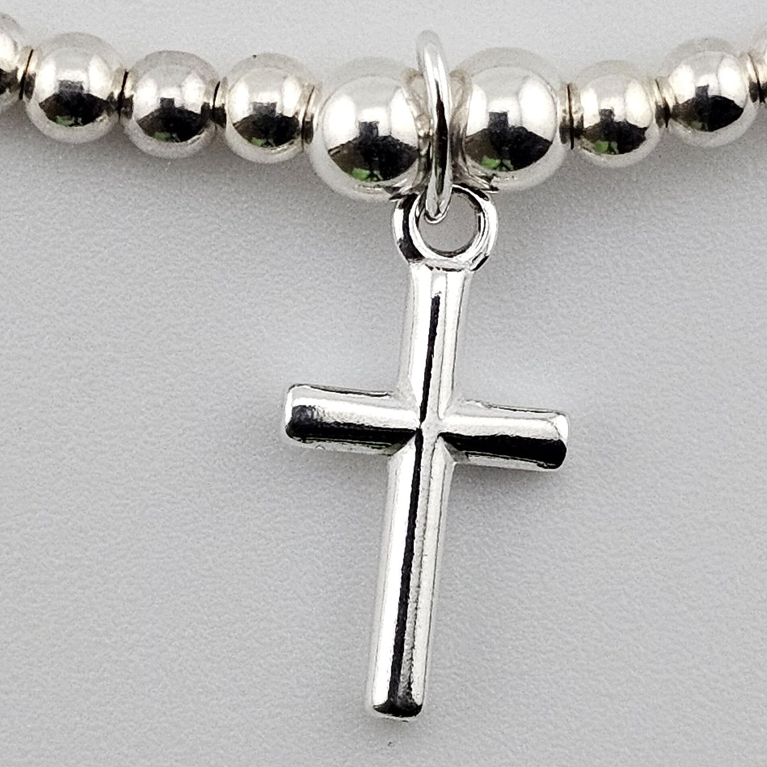 Close-up of sterling silver cross charm on beaded bracelet.