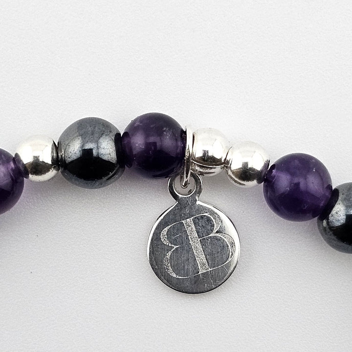 Bessie Bae logo tag attached to amethyst and hematite gemstone bracelet.