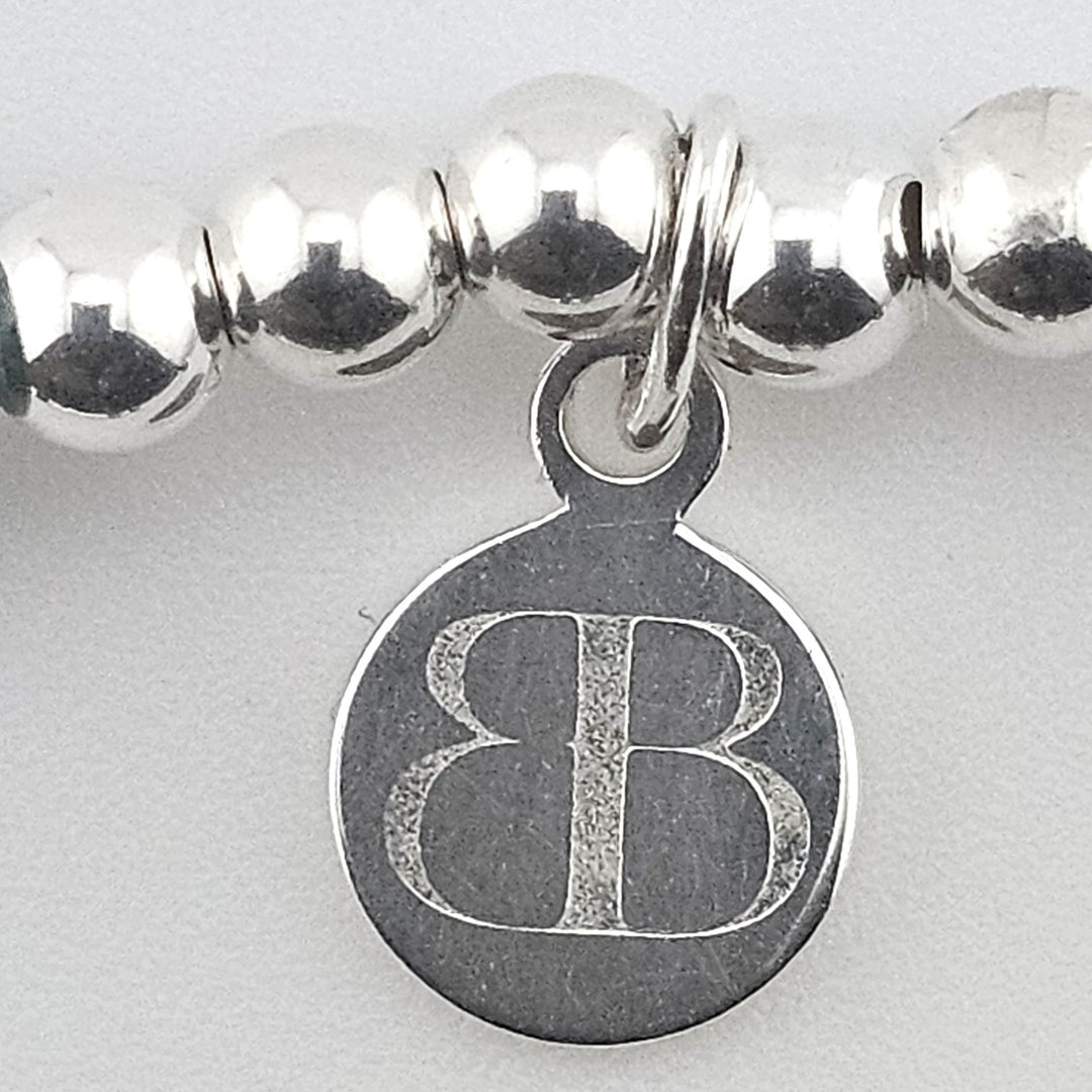 Close-up of Bessie Bae logo charm on bracelet.