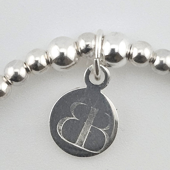Close-up of Bessie Bae logo charm on bracelet.