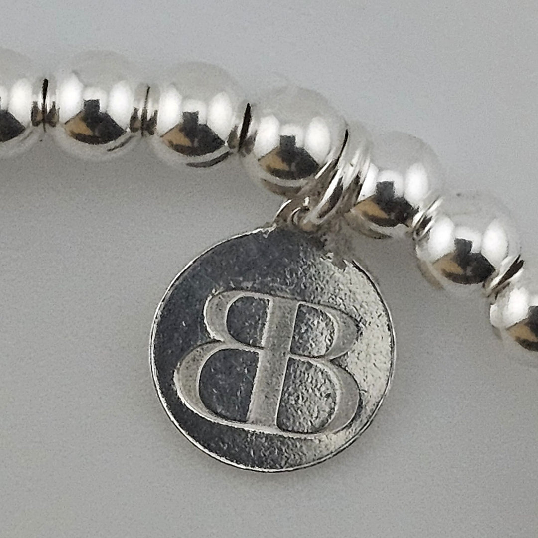 Close-up of Bessie Bae logo charm on bracelet.
