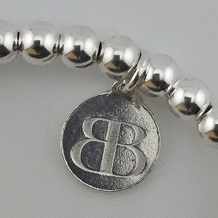 Close-up of Bessie Bae logo charm on bracelet.