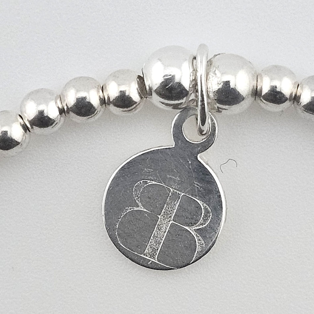 Close-up of Bessie Bae logo charm on bracelet.