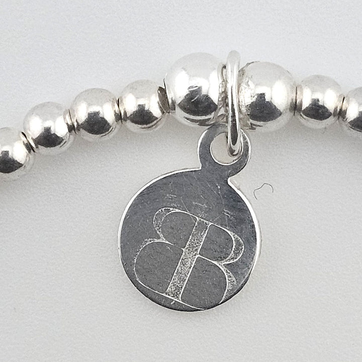 Close-up of Bessie Bae logo charm on bracelet.