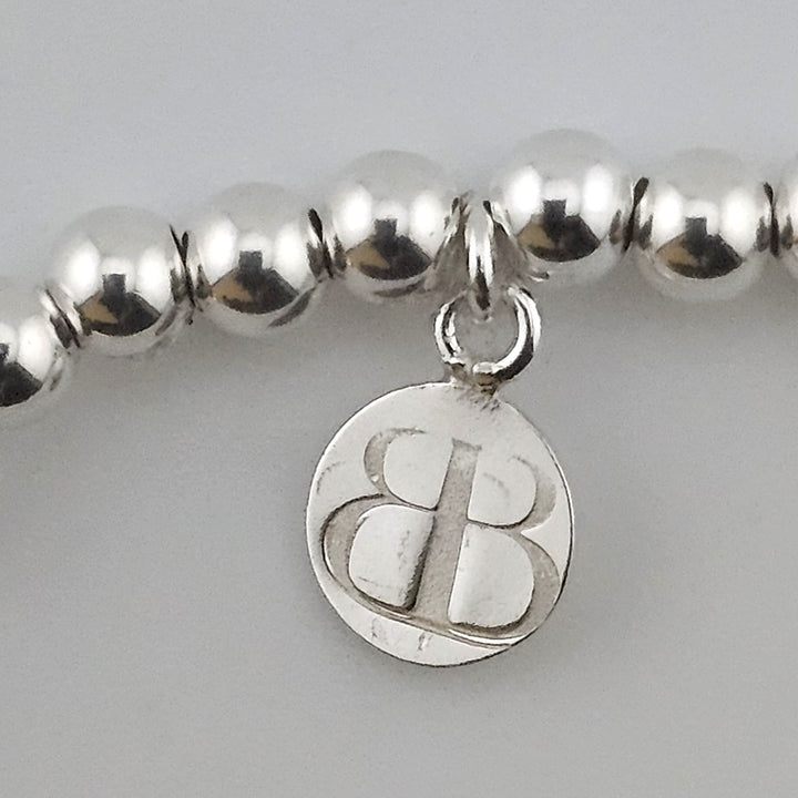 Close-up of Bessie Bae logo charm on bracelet.