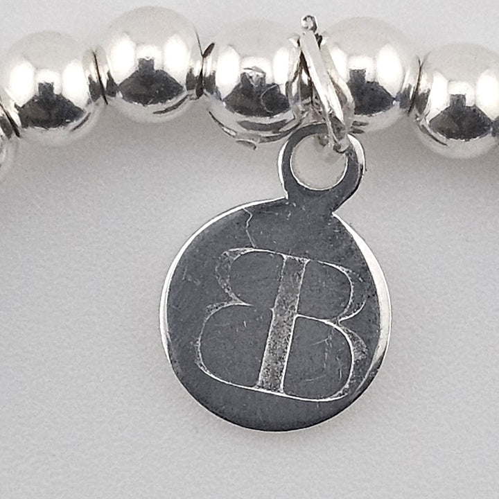Close-up of Bessie Bae logo charm on bracelet.