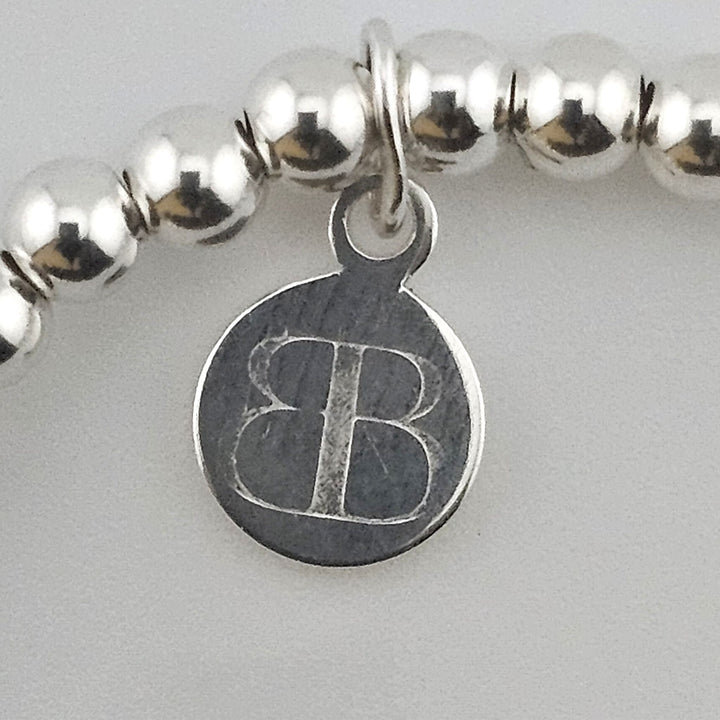 Close-up of Bessie Bae logo charm on bracelet.