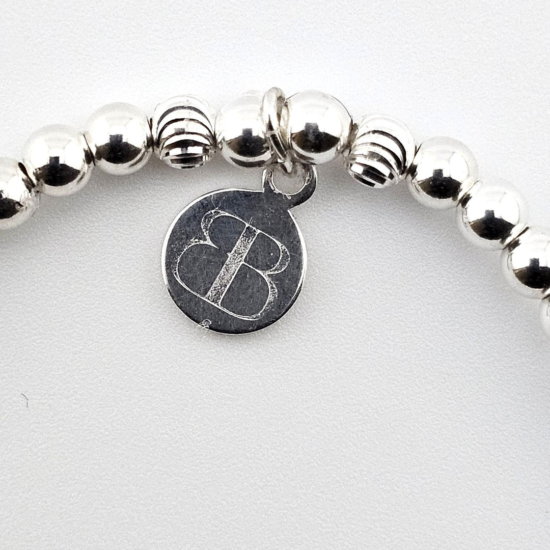 Bessie Bae logo tag attached to sterling silver cross charm bracelet.