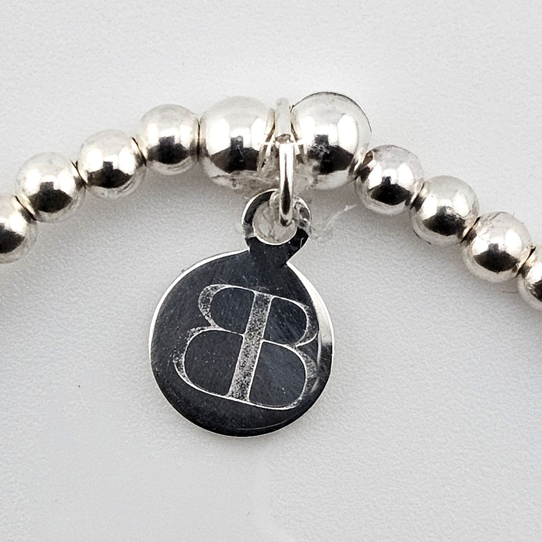 Bessie Bae logo tag attached to sterling silver Om charm bracelet.