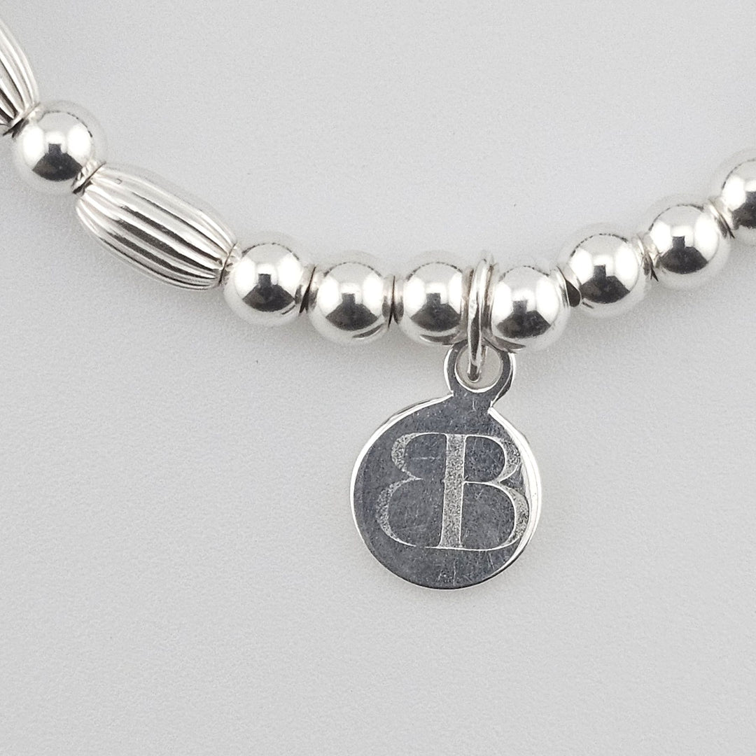 Bessie Bae signature logo charm attached to Sterling Silver and gemstone bracelet.