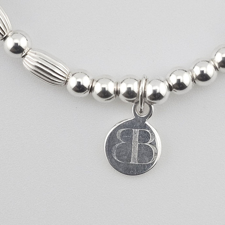Bessie Bae signature logo charm attached to Sterling Silver and gemstone bracelet.