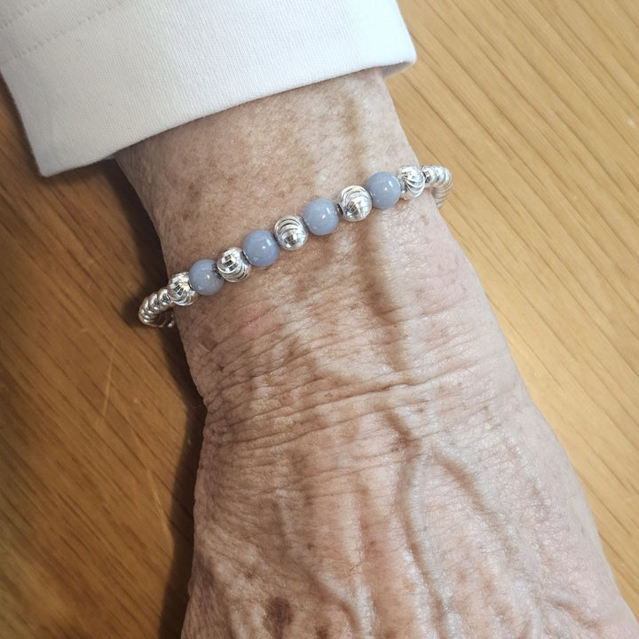 Wrist wearing a Bessie Bae silver and blue lace agate beaded bracelet on a wooden surface.