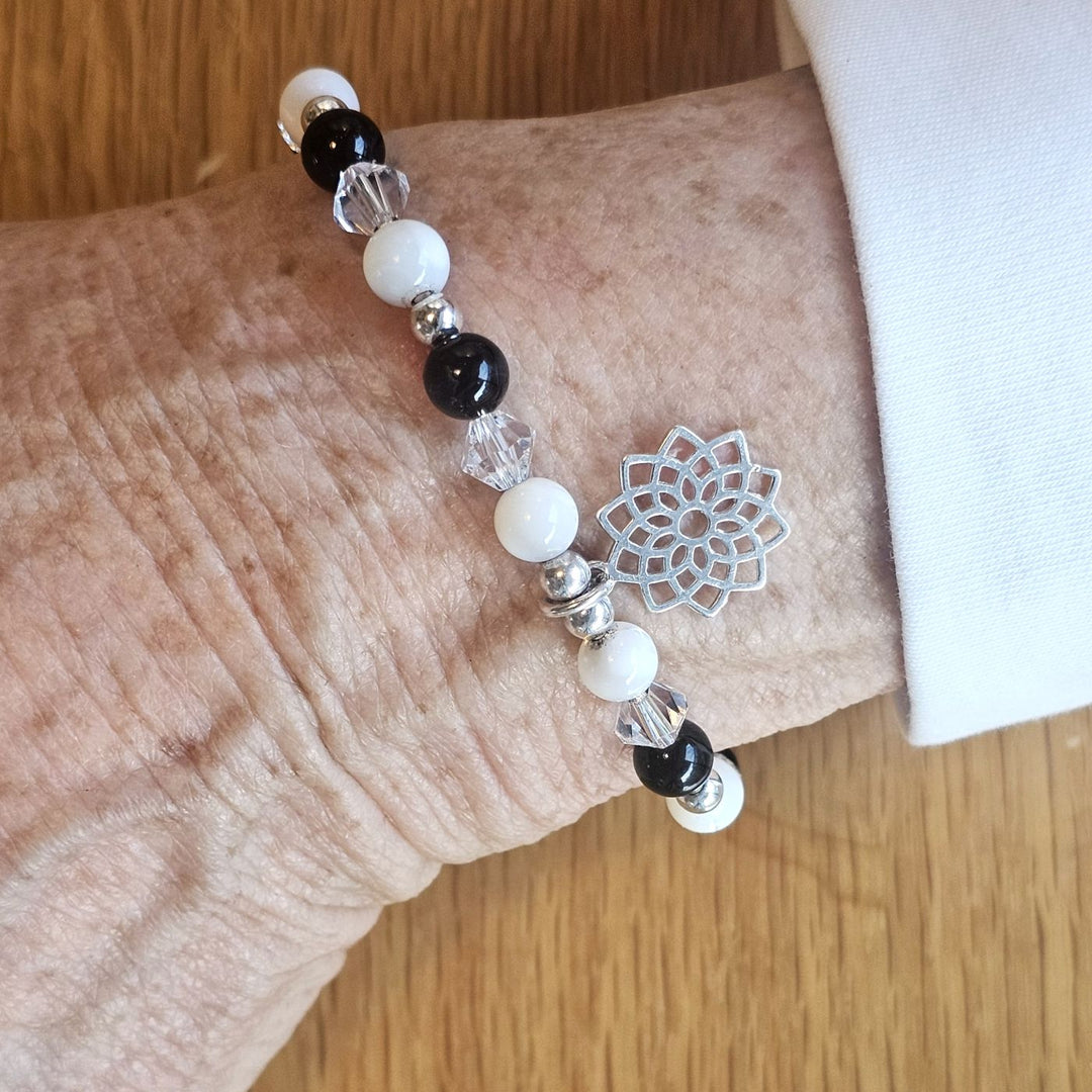 Wrist wearing a Bessie Bae silver floral charm bracelet with black, white, and crystal beads on a wooden surface.