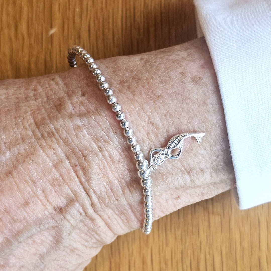Wrist wearing a Bessie Bae silver mermaid charm beaded bracelet on a wooden surface.