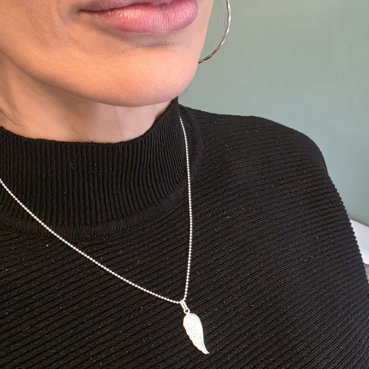 Sterling Silver Angel Wing necklace with sparkling guardian pendant worn on a woman’s neck over a black top.