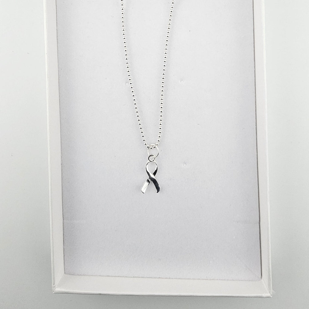 Sterling silver awareness ribbon necklace displayed inside a white jewellery gift box.