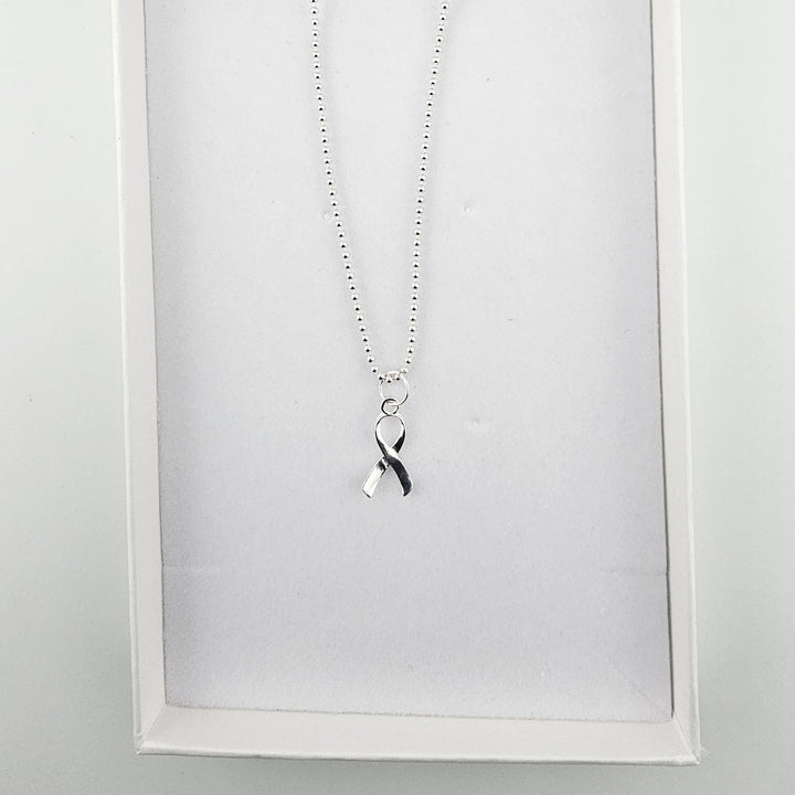 Sterling silver awareness ribbon necklace displayed inside a white jewellery gift box.