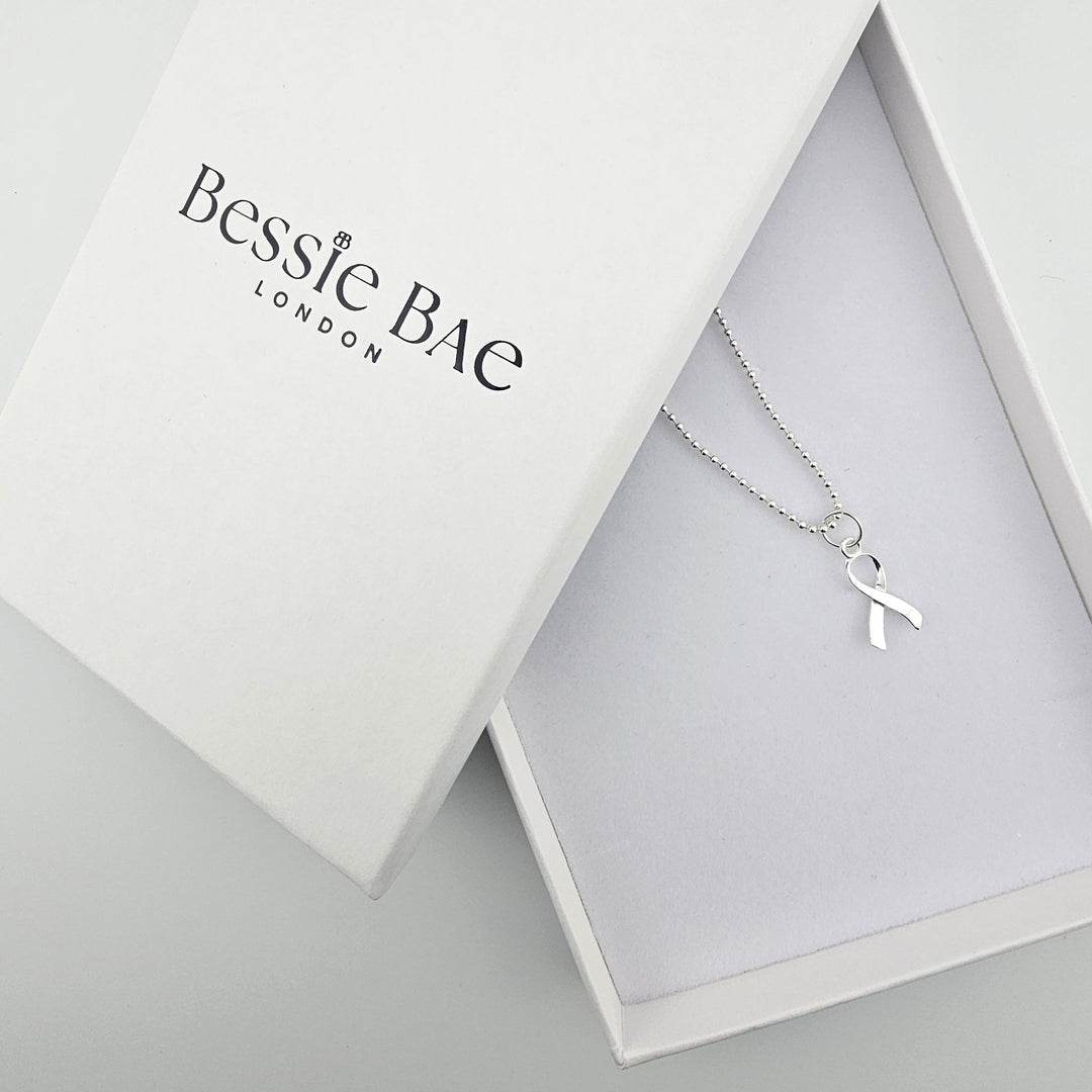 Sterling silver awareness ribbon necklace shown beside Bessie Bae branded packaging.