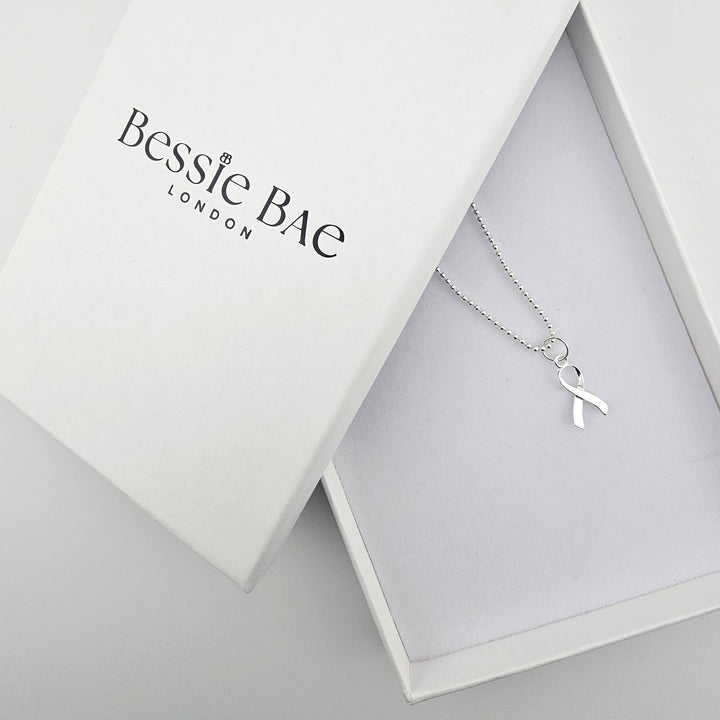 Sterling silver awareness ribbon necklace shown beside Bessie Bae branded packaging.