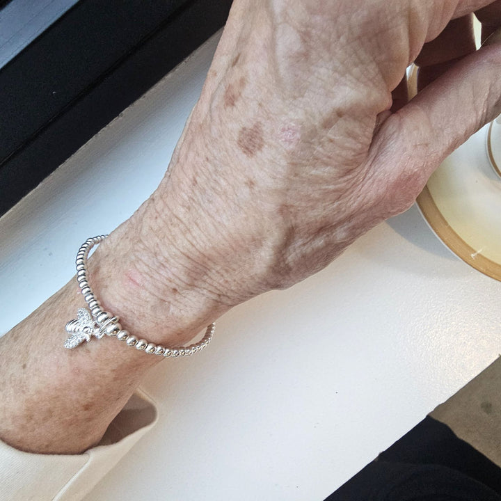 Sterling silver bee charm bracelet on wrist.