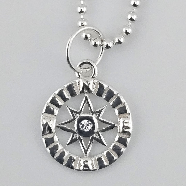 Close-up of a sterling silver compass star pendant with engraved detailing and a crystal centre.