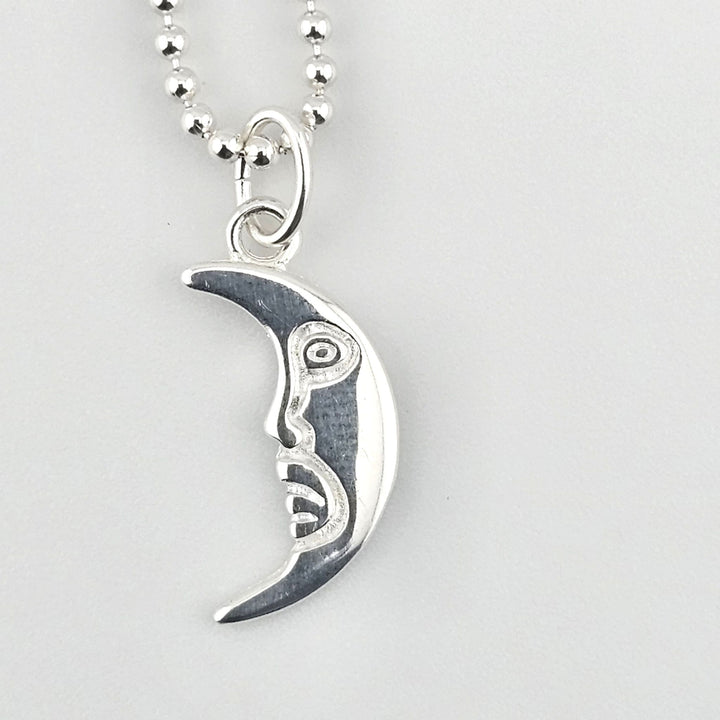 Close-up of sterling silver crescent moon pendant with sculpted face detail.