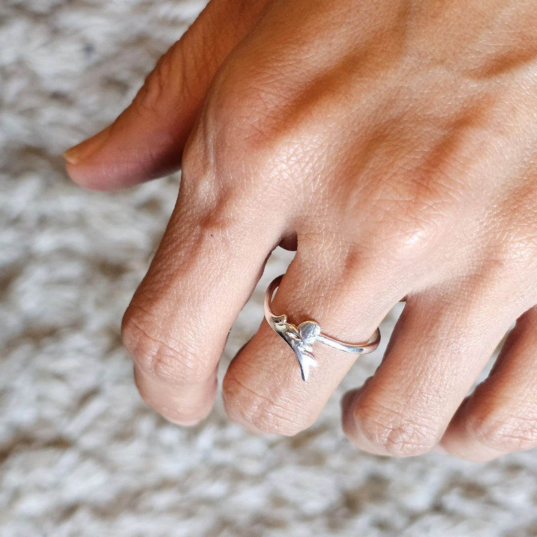 Adjustable sterling silver heart and arrow ring worn on a hand.