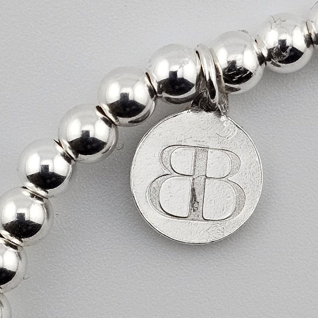 Bessie Bae silver logo charm attached to sterling silver beaded bracelet.