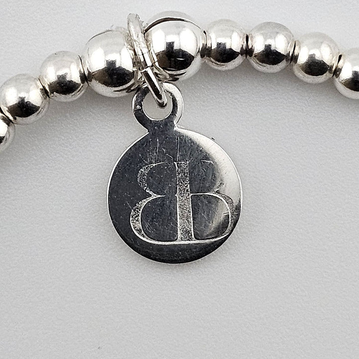 Close-up of Bessie Bae sterling silver logo charm on bracelet.