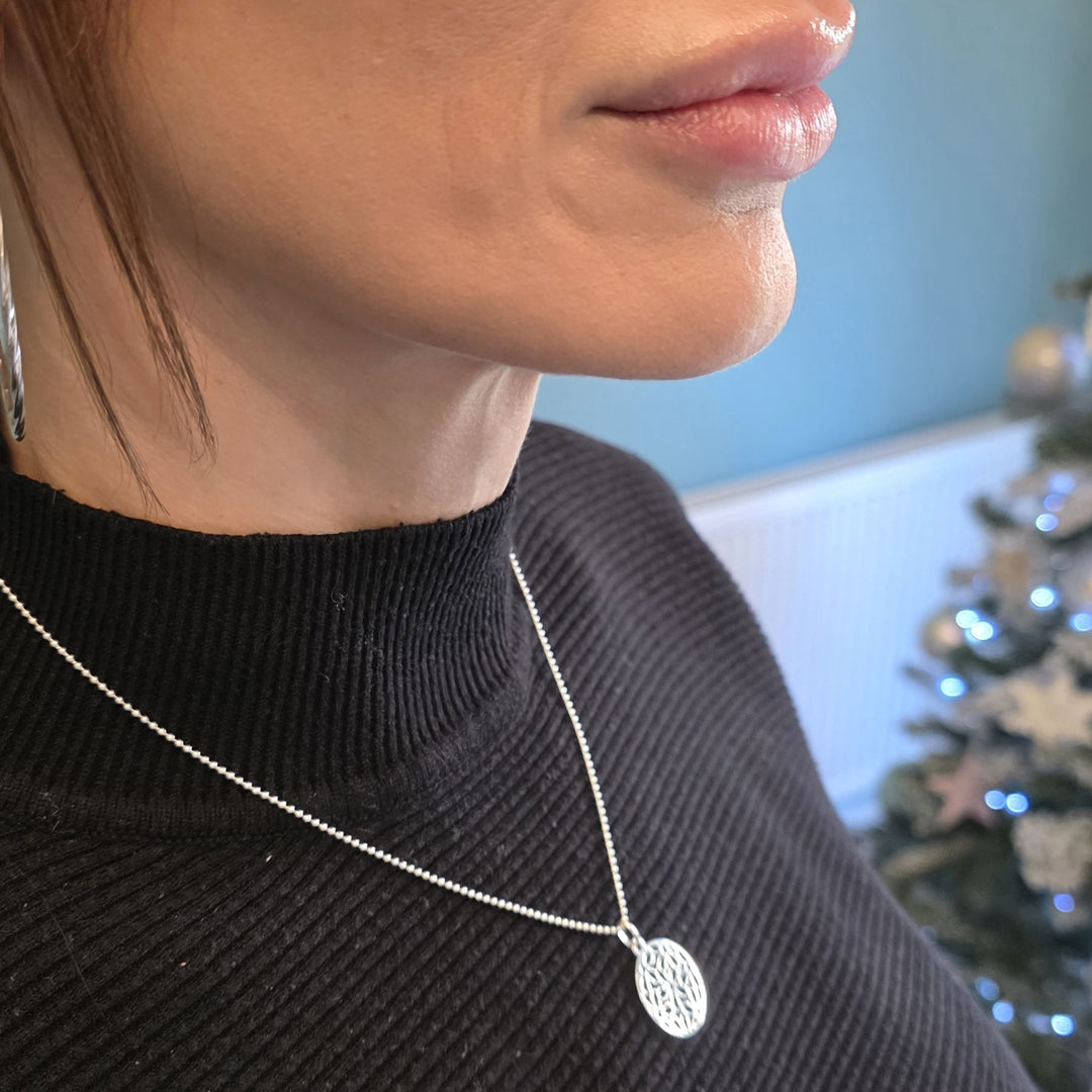 Sterling Silver mandala pendant necklace with intricate cut-out design worn on a woman’s neck over a black top.