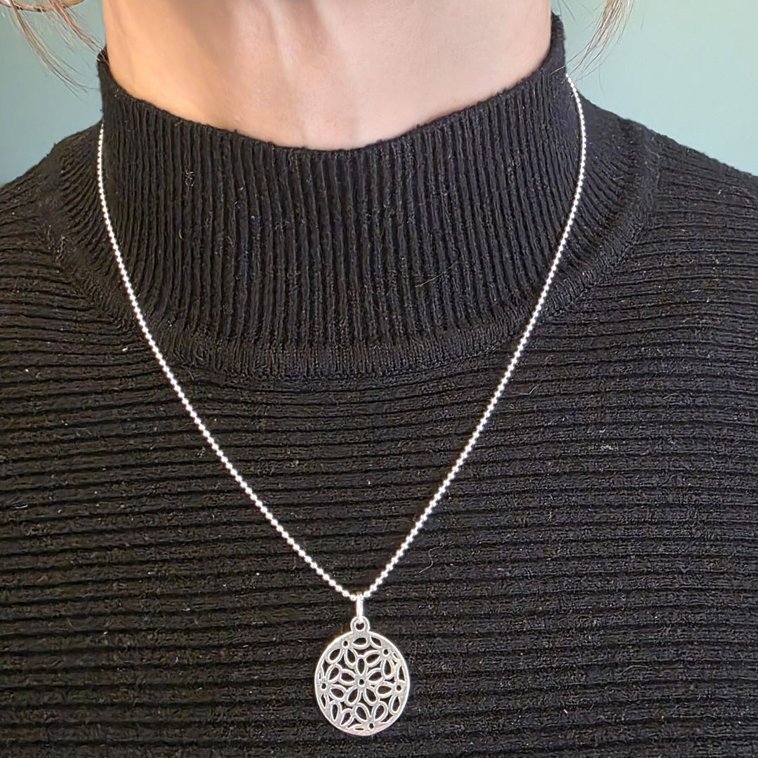 Sterling Silver mandala pendant necklace with intricate cut-out design worn on a woman’s neck over a black top.