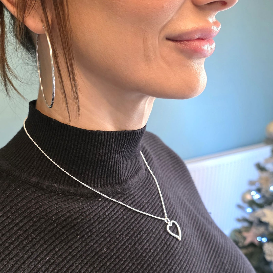 Sterling Silver open heart pendant necklace with gemstone accent worn on a woman’s neck over a black top.