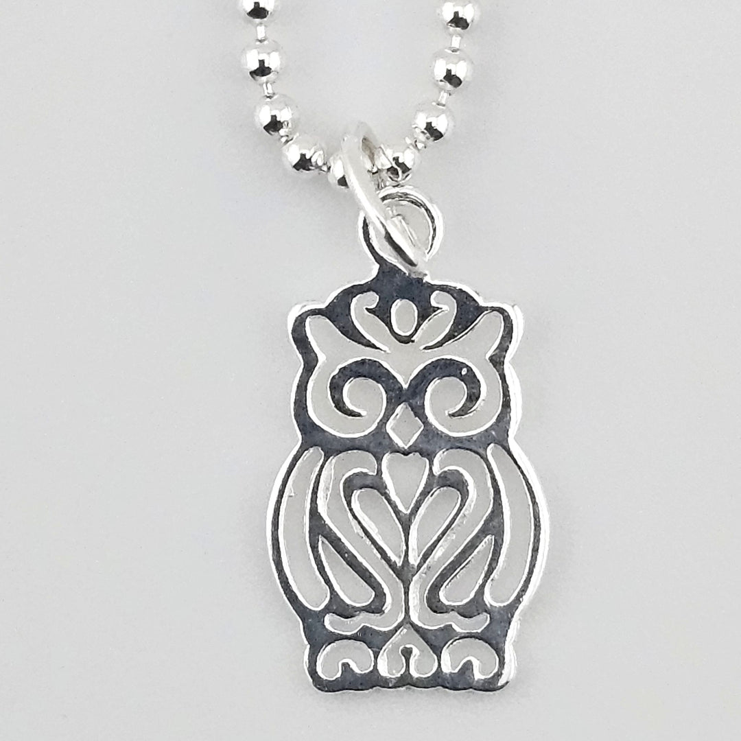 Close-up of a sterling silver owl charm with intricate cut-out detailing on a ball chain.