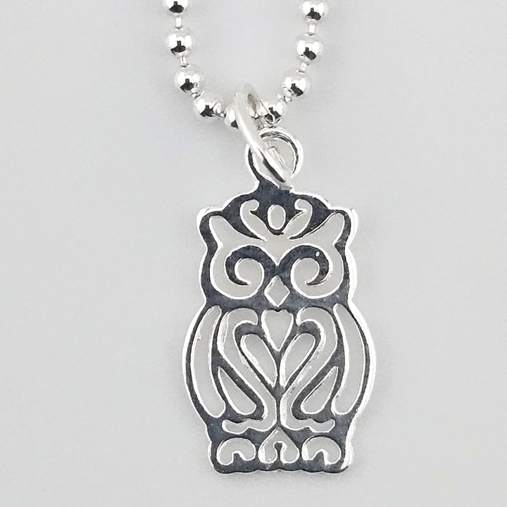 Close-up of a sterling silver owl charm with intricate cut-out detailing on a ball chain.