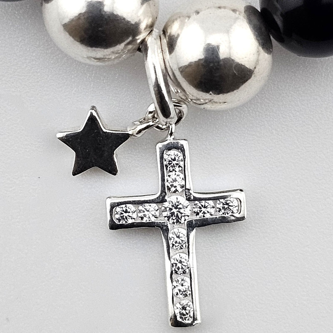 Close-up of sterling silver cross charm with crystal accents and small star pendant on black onyx and mother of pearl bracelet.