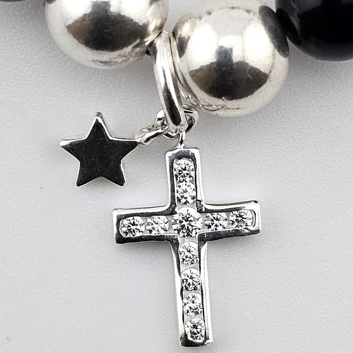 Close-up of sterling silver cross charm with crystal accents and small star pendant on black onyx and mother of pearl bracelet.
