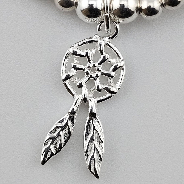 Close-up of silver dreamcatcher charm with feather detail on bracelet.