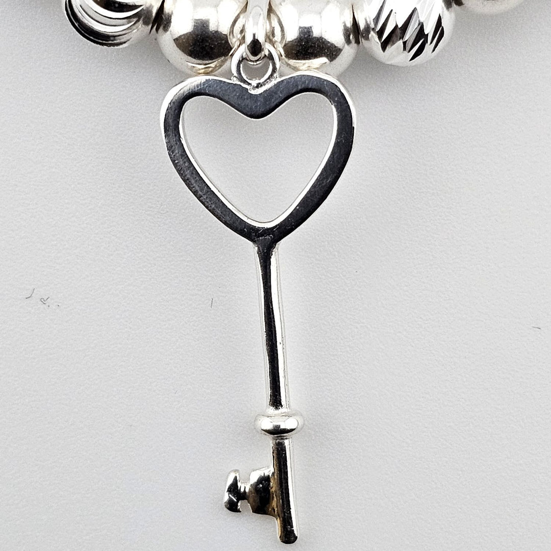 Close-up of sterling silver heart key charm on beaded bracelet.