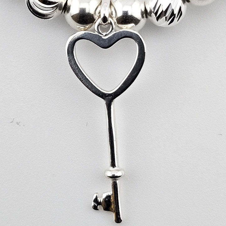 Close-up of sterling silver heart key charm on beaded bracelet.