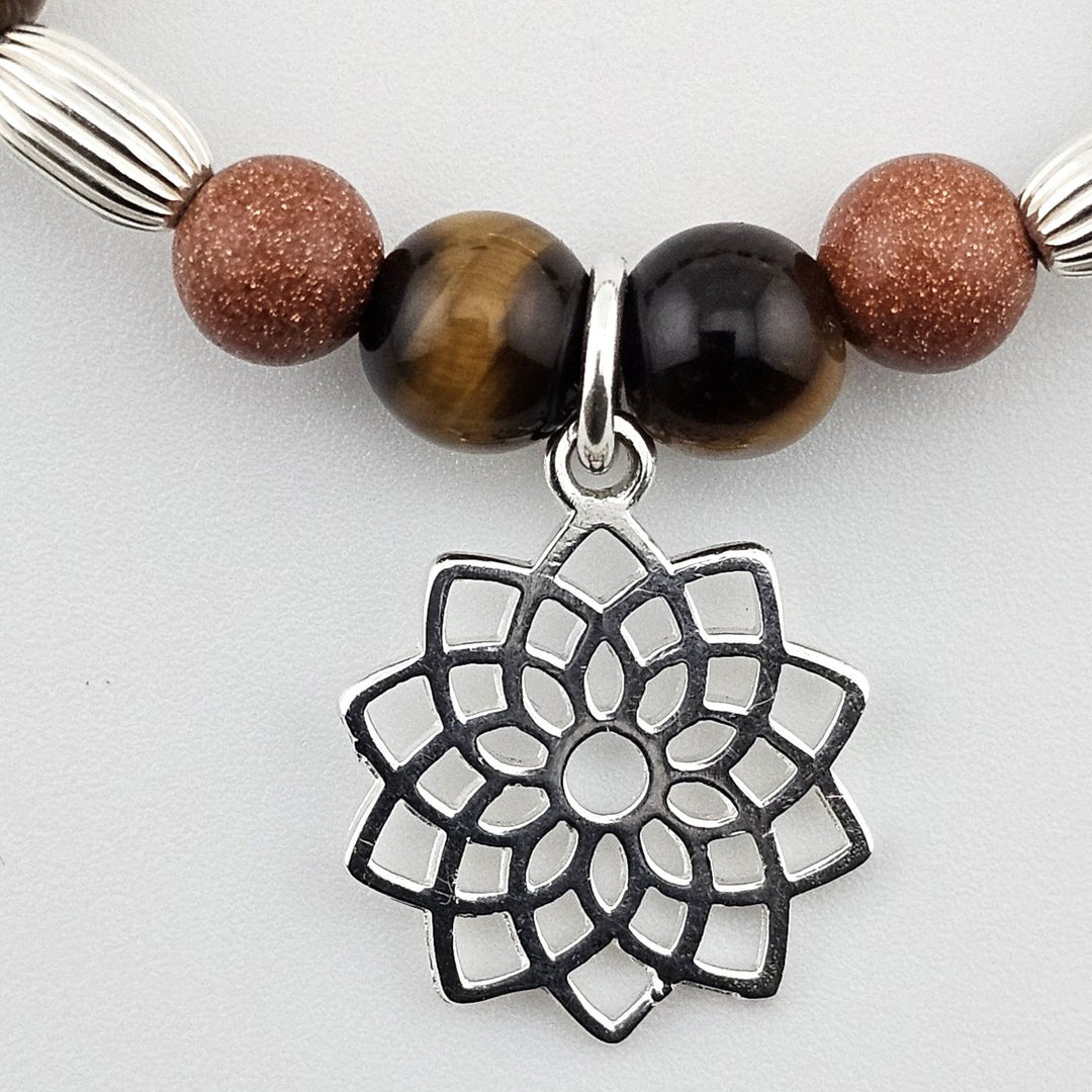 Close-up of sterling silver lotus charm on tiger’s eye and goldstone bracelet.