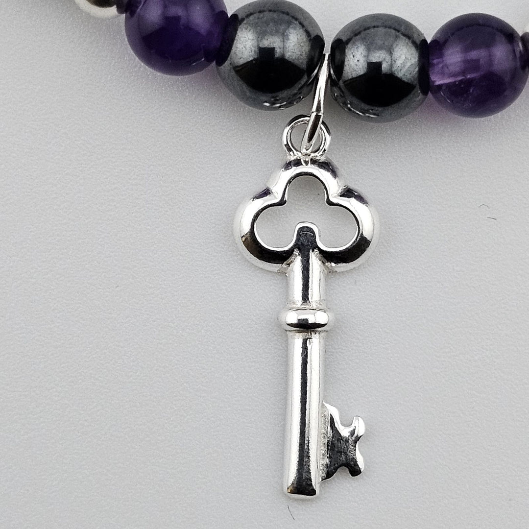 Close-up of sterling silver key charm on amethyst and hematite bracelet.