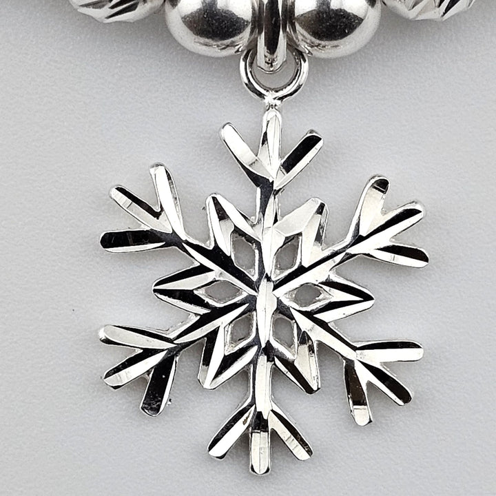 Close-up detail of sterling silver snowflake charm pendant on bracelet.
