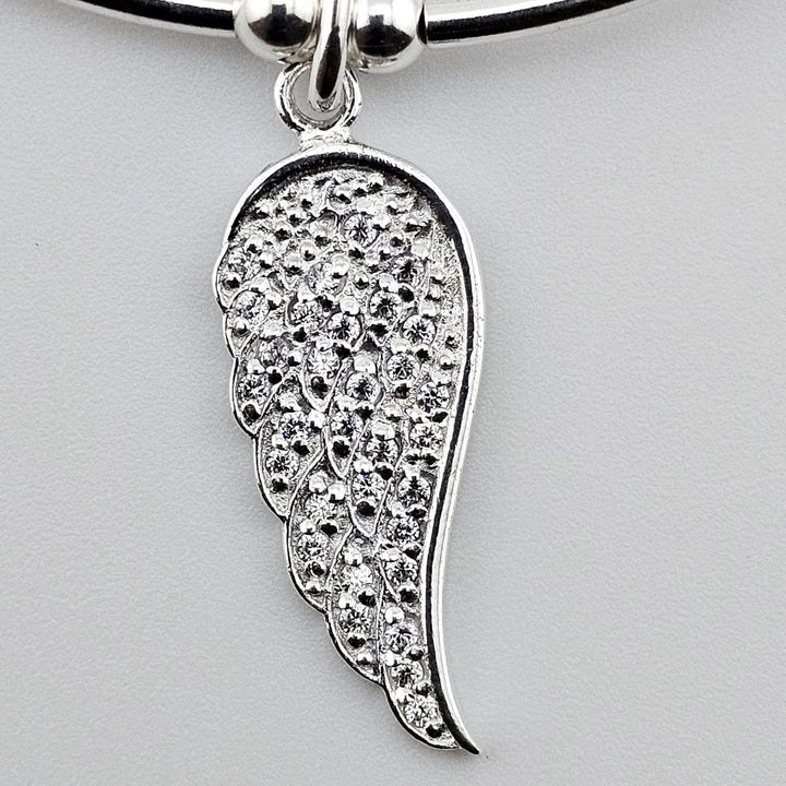 Close-up of angel wing charm with cubic zirconia crystals on silver bracelet.